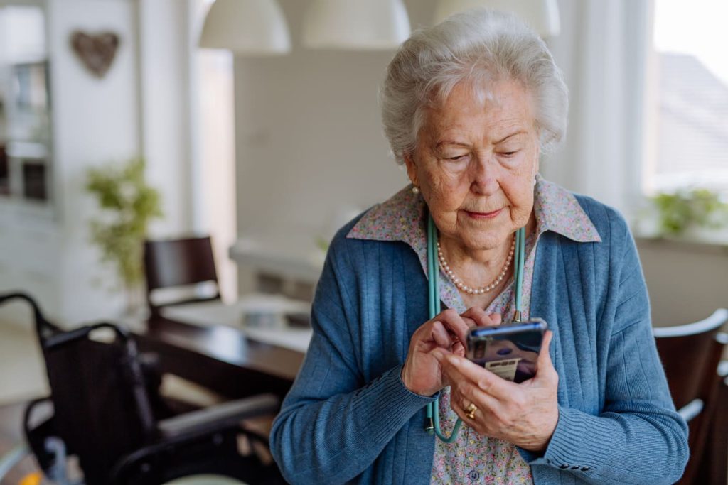 Eine betagte Frau hält ein Handy in der Hand. Sie telefoniert mit ihrer Angehörigen.