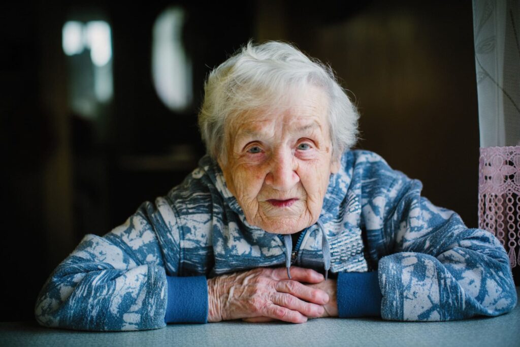 Portrait einer alten Frau an ihrem Wohnzimmertisch.